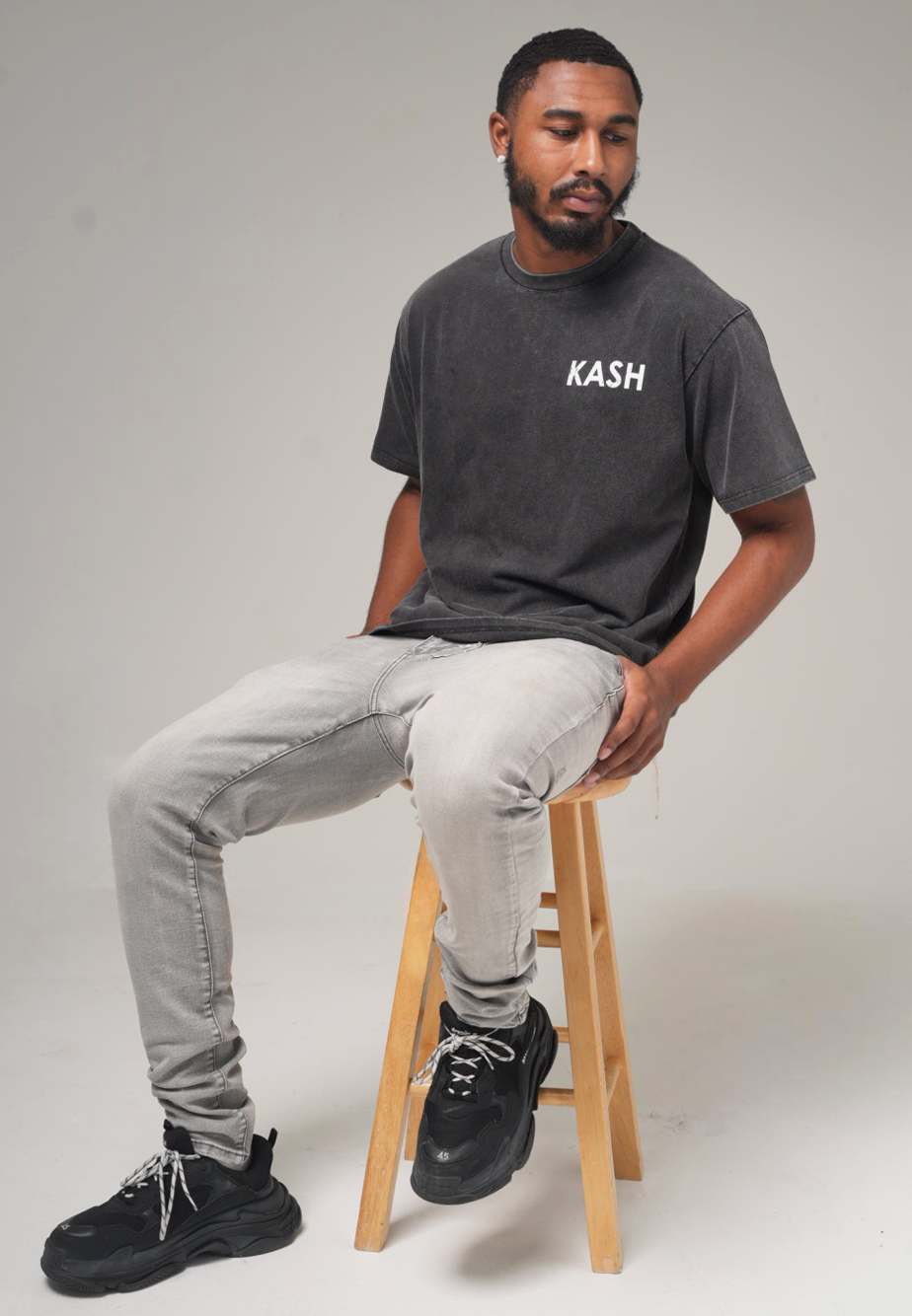 Model seated on a stool in the grey wash Kash tee and light jeans